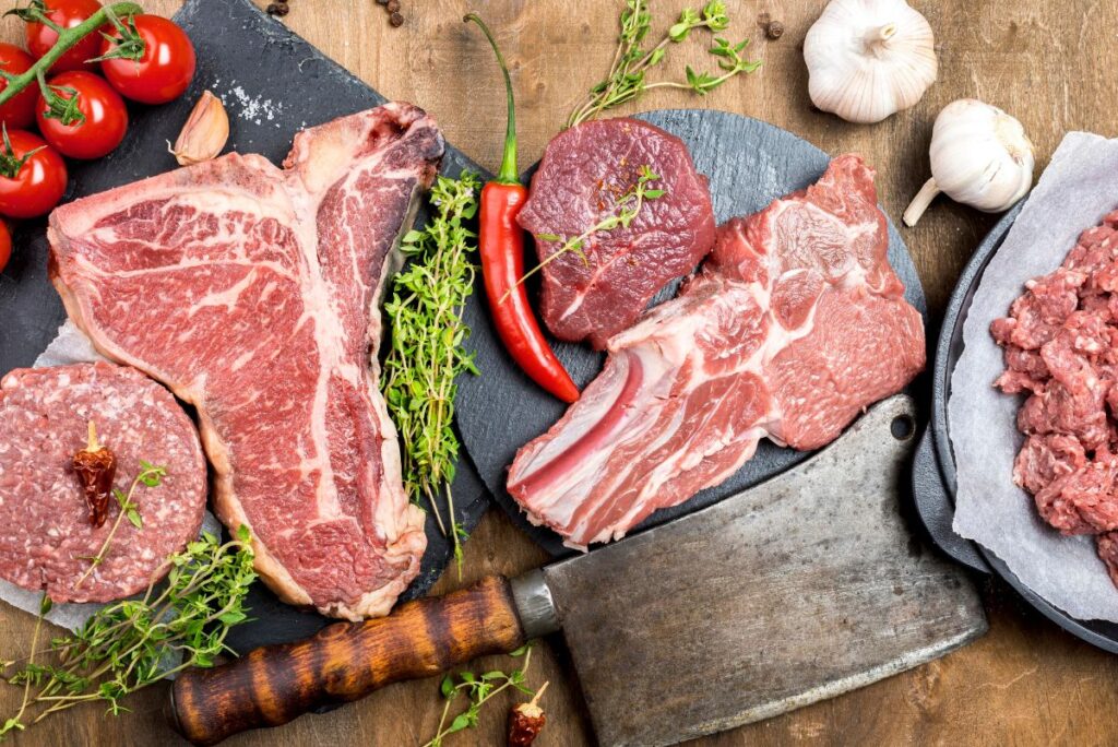 A range of different meats from steak to pork chops laid out on a wooden chopping board