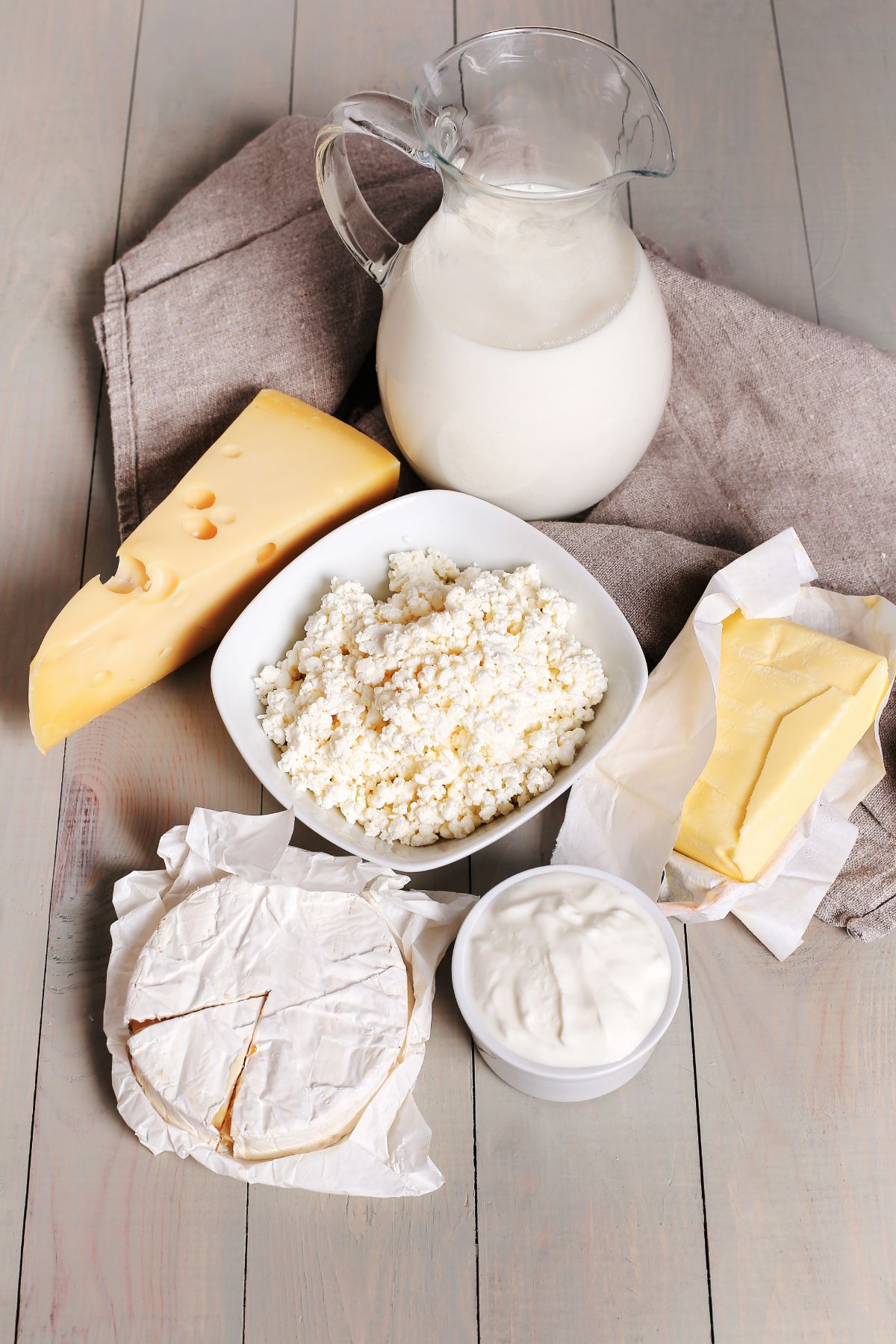A selection of cheeses and a jar of cream, laid out on a wooden table